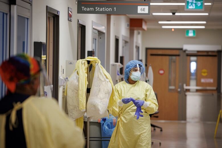 A nurse in a personal protective equipment walks down a hospital corridor.