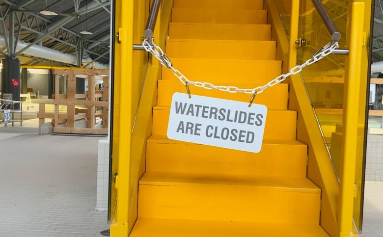 A stair leading up to a waterslide with a chain across it and a sign that says Waterslides are Closed. 