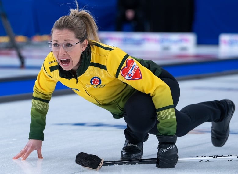 A woman slides on the ice in curling gear. 