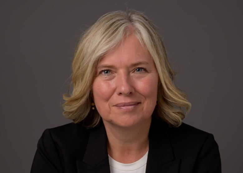 A woman wearing a black blazer looks into the camera.