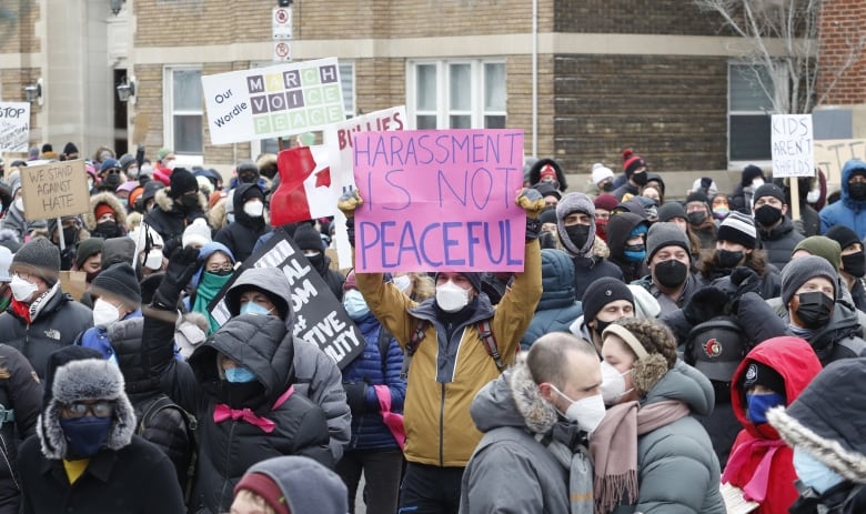 A crowd of people outside in winter coats, some holding signs.