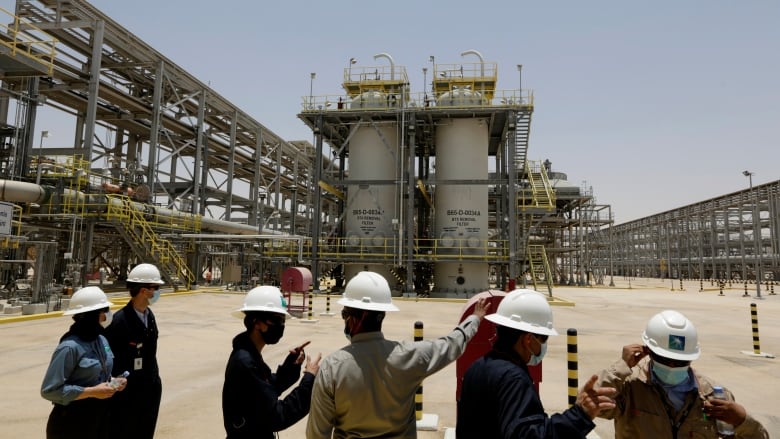 Several people wearing hard hats are pictured at an oil production site.