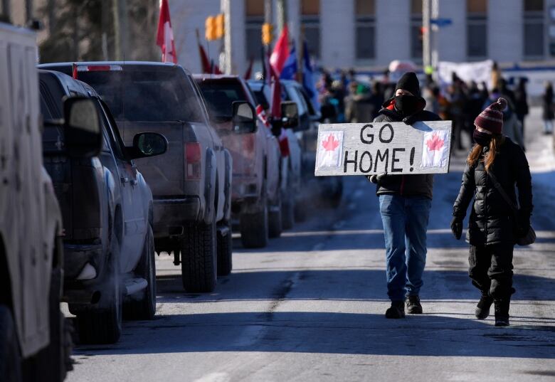 A resident holds a sign towards protesters as they participate in a counter protest to stop vehicles from driving in a convoy en route to Parliament Hill, on the 17th day of a protest against COVID-19 measures that has grown into a broader anti-government protest, in Ottawa, Sunday, Feb. 13, 2022. THE CANADIAN PRESS/Justin Tang