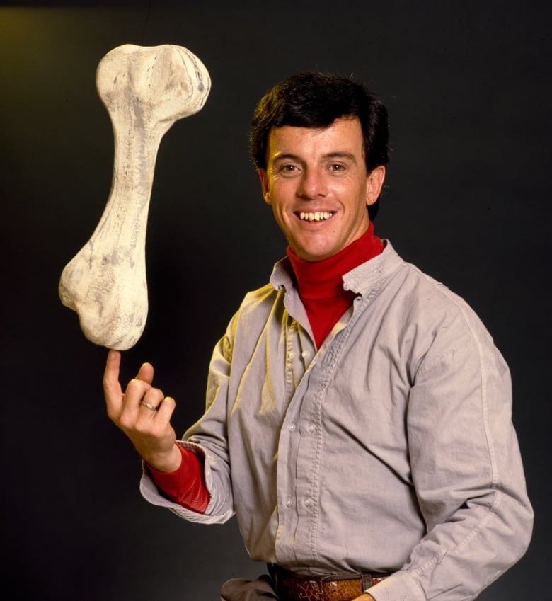 A man sits for a portrait, holding a large animal bone.