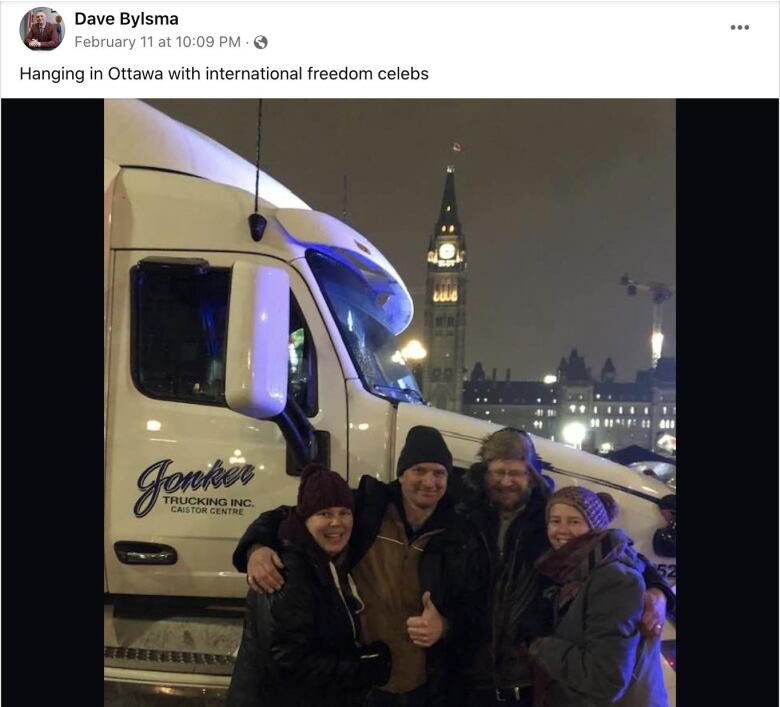 Four people stand in front of a truck.