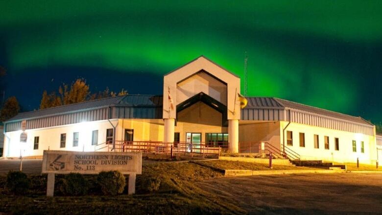 Green and blue auras cover the sky behind building.