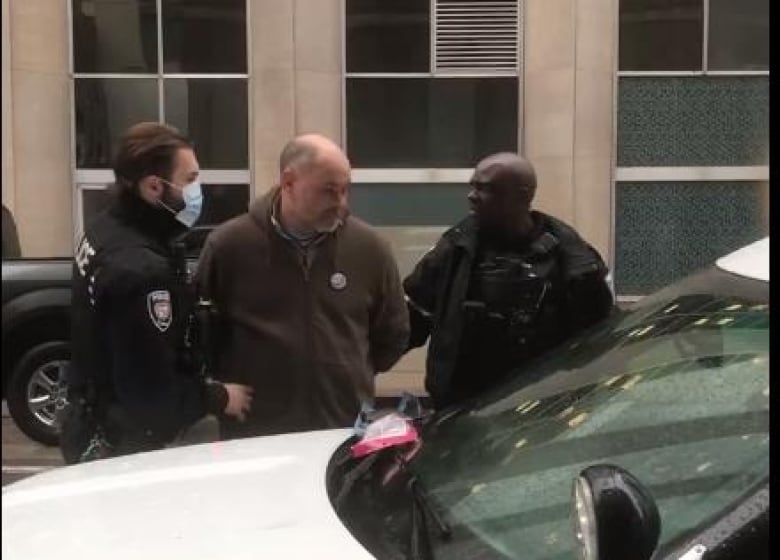 A man led toward a police vehicle by two officers.