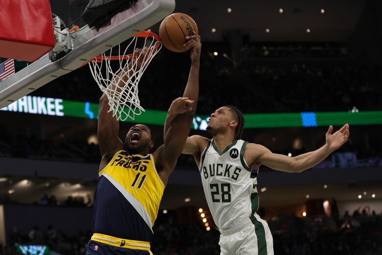 Two men at a basketball net. One is wearing an Indiana Pacers Jersey, the other is wearing a Milwaukee Bucks jersey