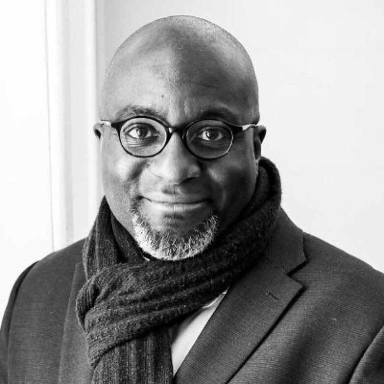 A black and white photo of  a bald Black man wearing round glasses and a scarf