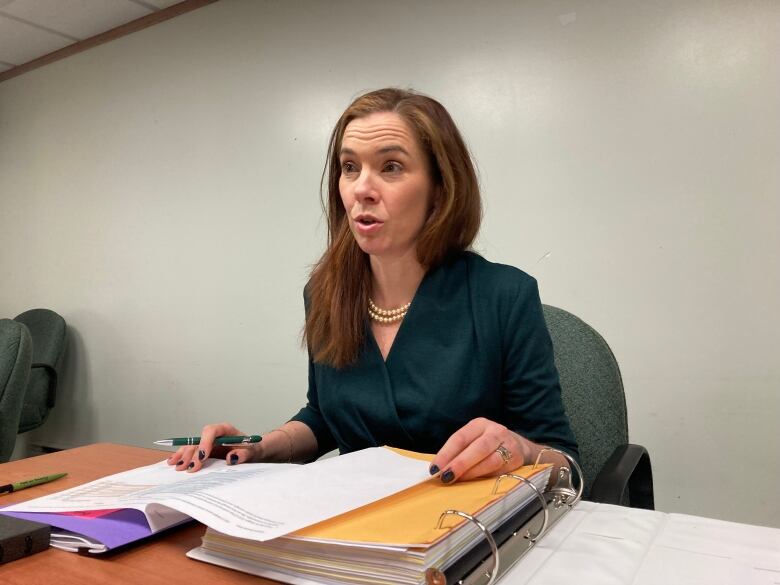 A woman sits behind a table with an open binder in front of her.