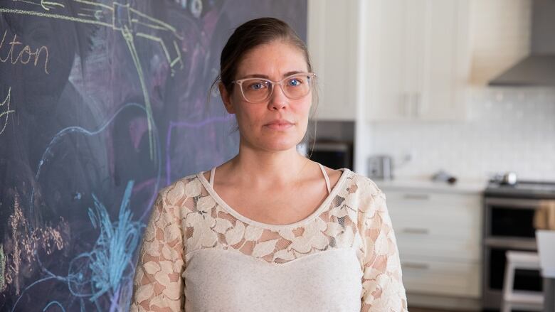 Woman in white top and glasses stands in her house.