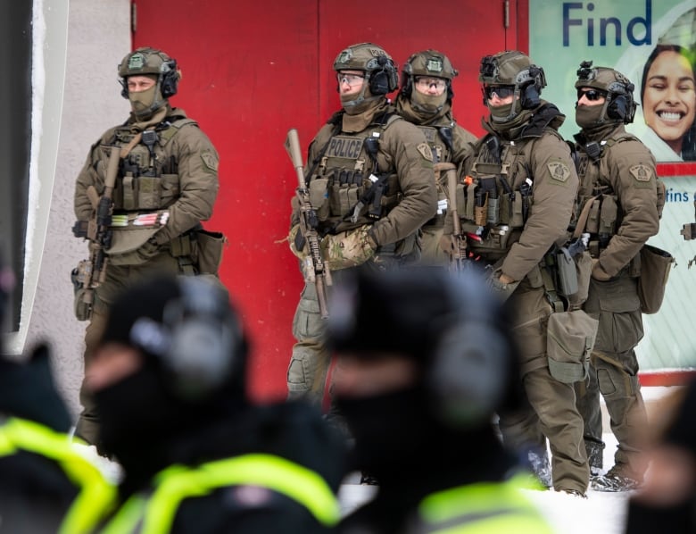 RCMP tactical officers stand behind uniformed officers as they prepare to clear protesters from a blockade of vehicles on Rideau Street, as police aim to end an ongoing protest against COVID-19 measures that has grown into a broader anti-government protest, on its 22nd day, in Ottawa, on Friday, Feb. 18, 2022.