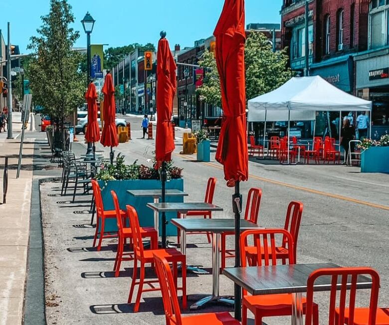 Tables with red umbrellas are set out on a downtown street. 