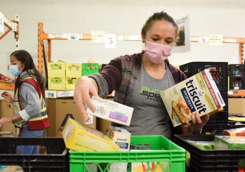 A woman puts food items into a plastic crate.