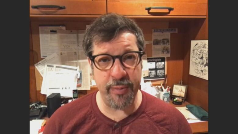 A portrait of a man sitting at a cluttered desk.