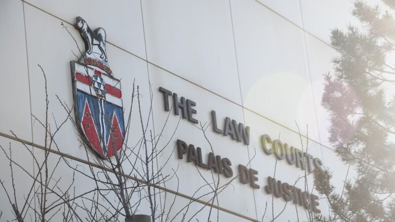 Black letters reading THE LAW COURTS PALAIS DE JUSTICE are mounted on large white tiles on the side of a building next to the Yukon territorial logo