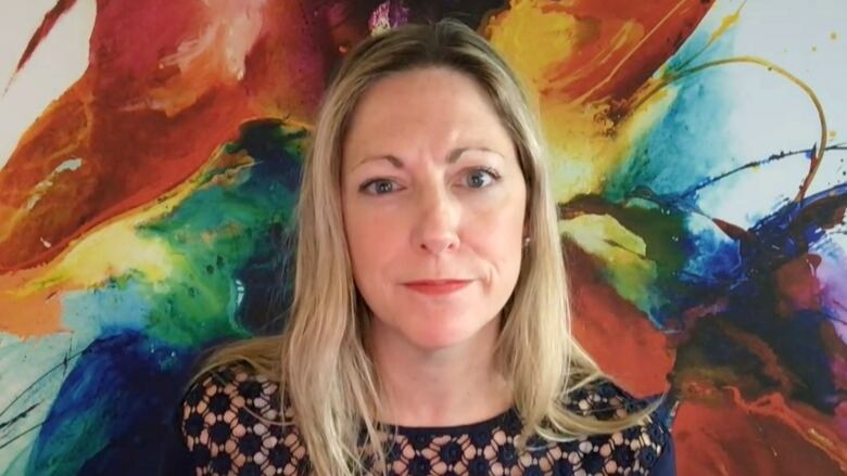 A woman with blonde hair sits in front of a mural showing explosions of paint on a white background.