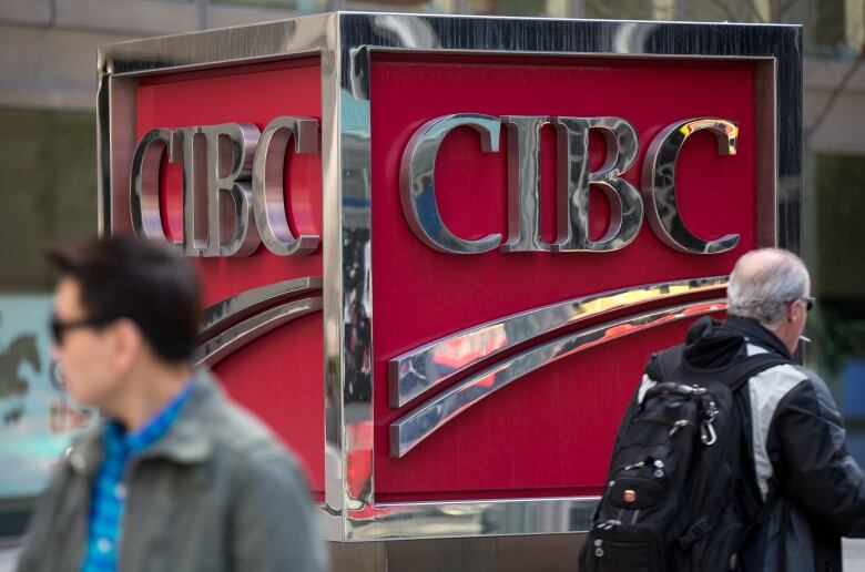 Pedestrians walk in front of a CIBC logo