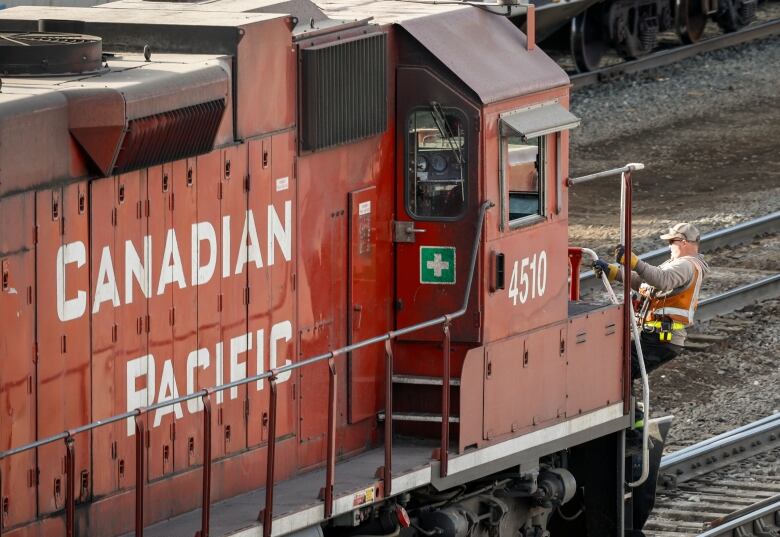 A railway worker boards the front of a red locomotive.