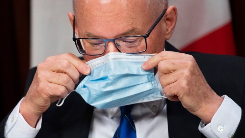 A man with eyeglasses puts on a blue mask.