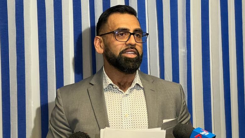 A man stands in front of a podium to answer media questions.