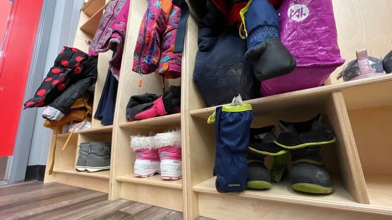 A wooden coat cubby full of colourful jackets, mitts and boots. 