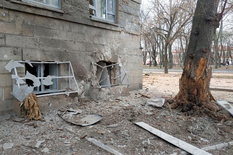 Windows of a concrete building are shattered with debris all around.