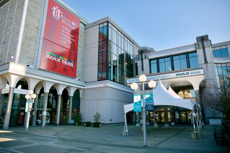 The exterior of the Royal B.C. Museum with exterior globed lighting, a pavillioned entrance and signs advertising an IMAX experience.