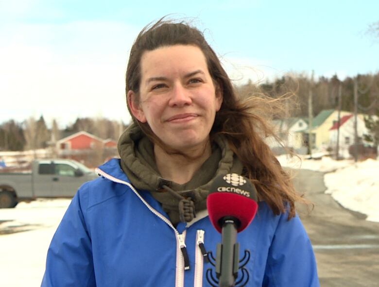 Fiona Humber wearing a blue jacket smiles while speaking into a CBC microphone outside. There's snow in the background. 