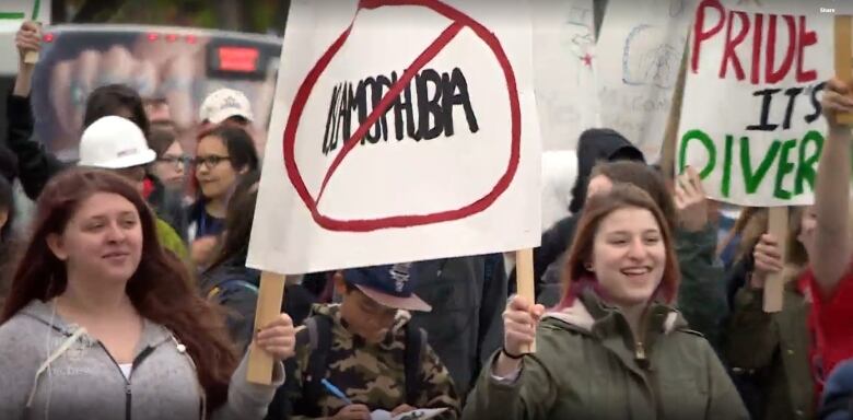 Two young people walking in a large group hold a sign with the word 