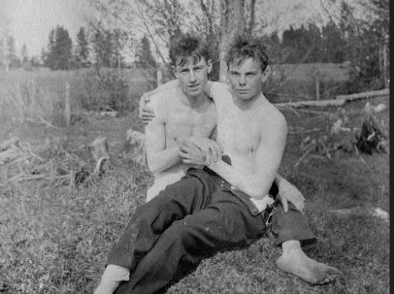 A black and white photo of two men, with one sitting on the other, and holding hands.