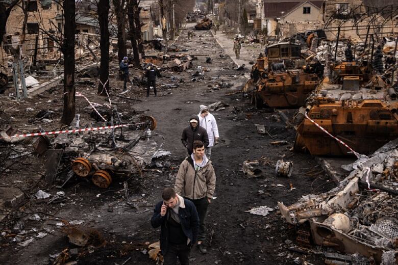 People walk along a heavily damaged street strewn with rubble, debris and destroyed vehicles.