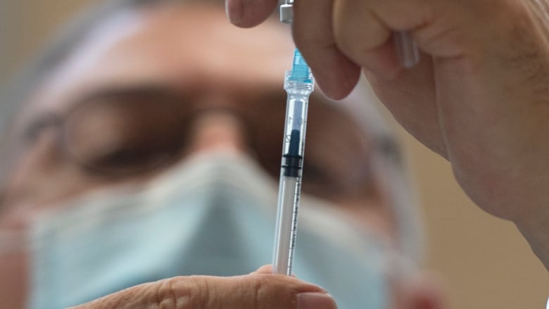 A man wearing a medical mask draws a vaccine dose from a vial.