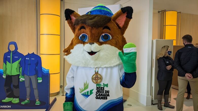 The mascot for the 2023 Canada Winter Games, with a large fox head, a white and green jersey, and a quillwork medallion around their neck. 