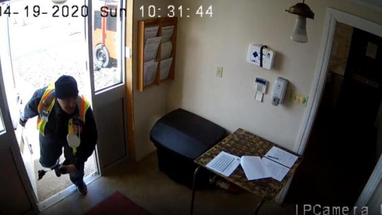 An image from a security camera shows a man in a safety vest coming through a door.