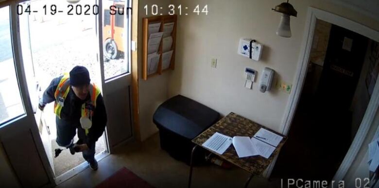 An image from a security camera shows a man in a safety vest coming through a door.