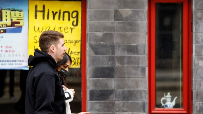 Pedestrians walk by a 'hiring' sign of a Toronto business on April 11, 2022.