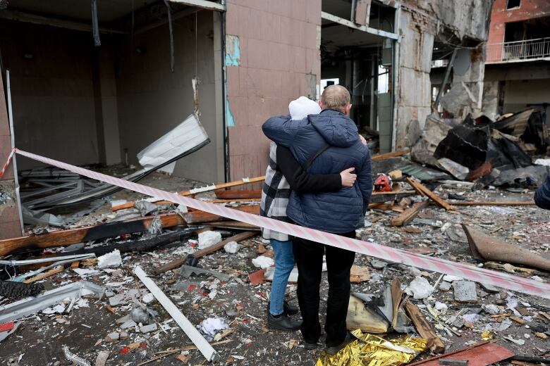 Two people hug hold onto each other amongst the ruins of a building.