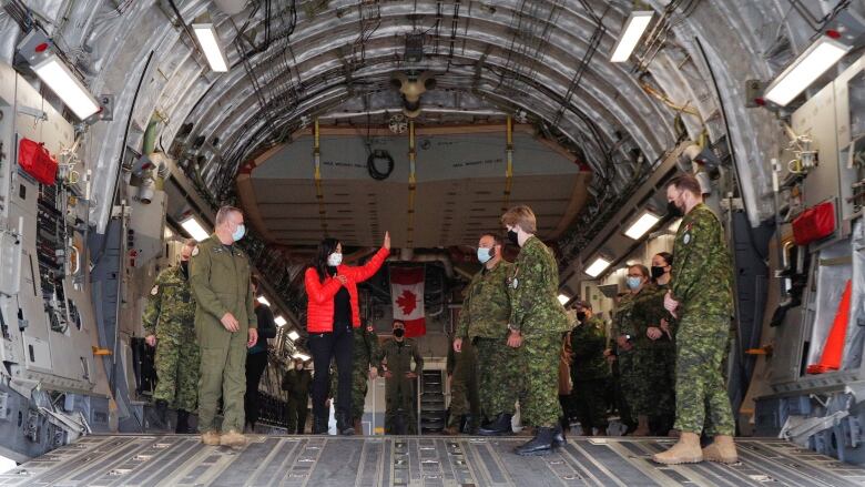 Soldiers stand with a woman in a red jacket in the cargo hold of an aircraft.