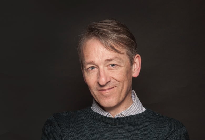 Head and shoulders photo of man in green sweater and striped shirt.