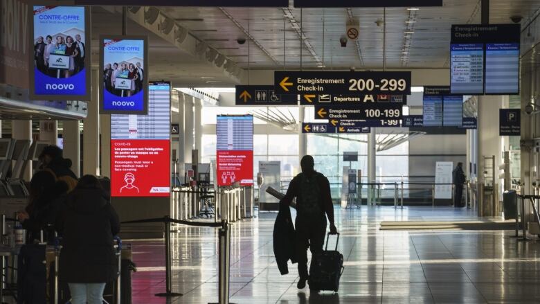 A person pulling a suitcase walks through a dimly lit airport. 