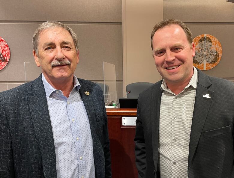 Two men in jackets and dress shirts smiling.