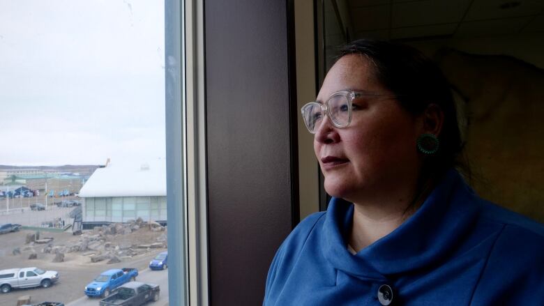 A woman stands inside, looking out a window.