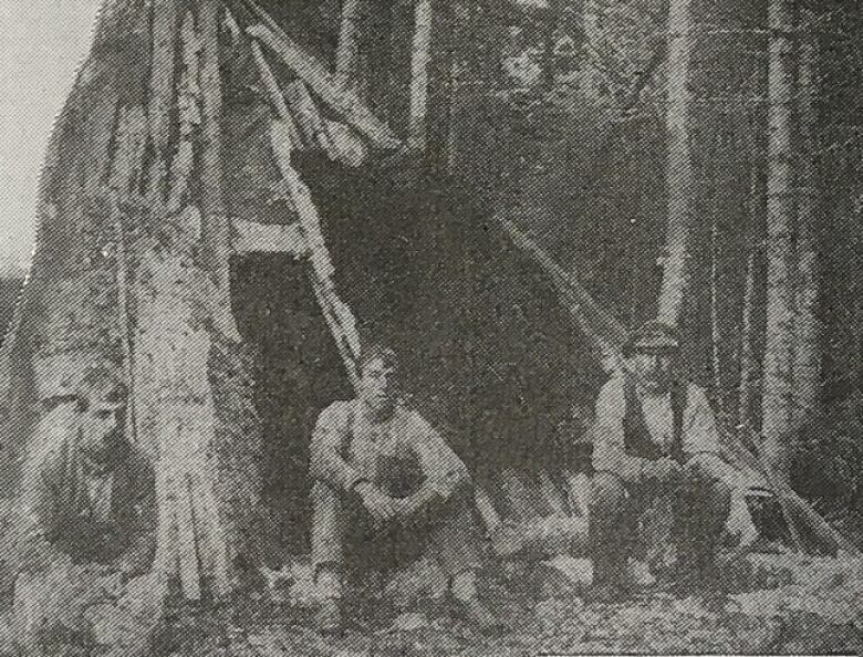 Three men sit in front of a teepee in an old black and white photo