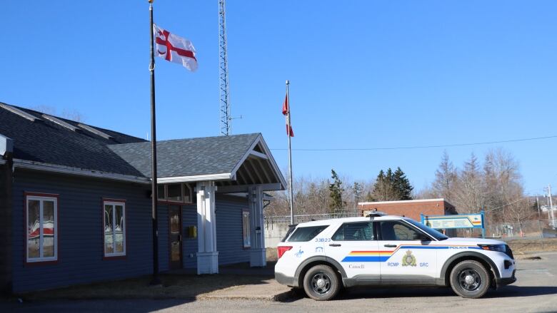 A white RCMP vehicle sits in front of a one-level building with a Canadian and a Mi'kmaw flag.