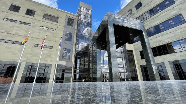 A multi-storey stone building with flags of Canada, New Brunswick and Moncton flying on poles near its entrance.