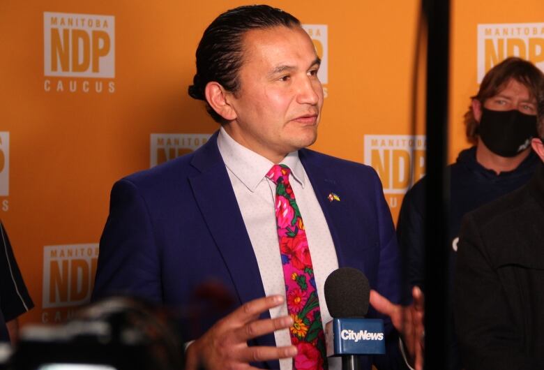 A man speaks in front of an orange backdrop that says 