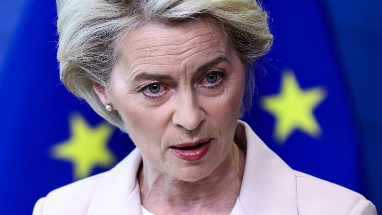 A blonde woman stands in front of a European Union flag.