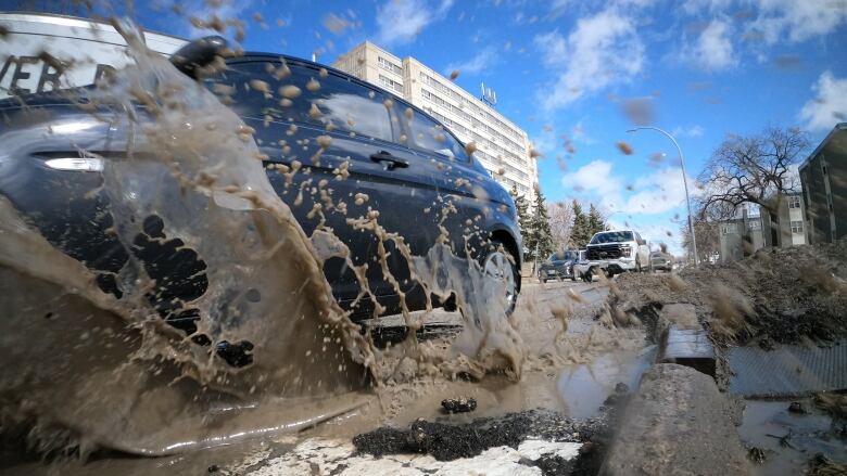 A vehicle splashes through water as it drives over a pothole.