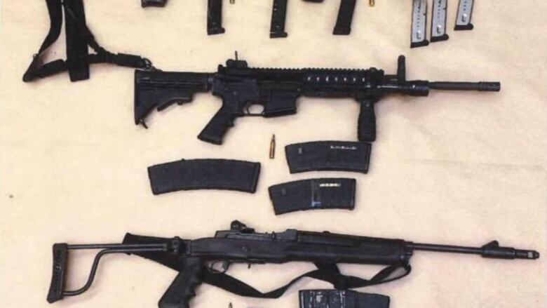 An arrangement of firearms including rifles and pistols are laid out on a beige background